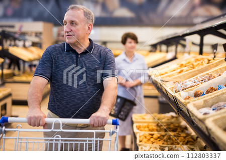 Elderly retired man buying bread and pastries in grocery section of the supermarket Elderly retired man buying bread and pastries in grocery section of the supermarket 112803337