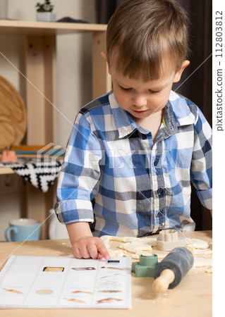 Two-year-old boy making his first cookie with a recipe book for toddlers. 112803812