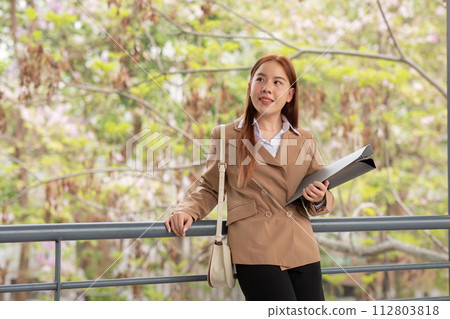 Young beautiful successful business woman outside office building, successful Asian woman smiling standing with documents 112803818