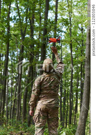 Elite military unit, equipped with state-of-the-art technology including a drone, strategically navigates and surveys dangerous wooded terrain, showcasing their precision, cooperation, and specialized 112803846