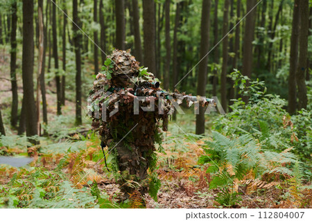 A highly skilled elite sniper, camouflaged in the dense forest, stealthily maneuvers through dangerous woodland terrain on a covert and precise mission 112804007