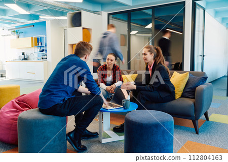 Multiethnic startup business team on meeting in a modern bright open space coworking office. Brainstorming, working on laptop. Group of coworkers walking around in motion blur 112804163