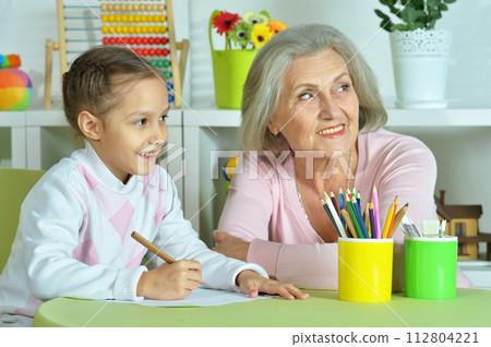 Portrait of grandmother with granddaughter drawing at home  112804221
