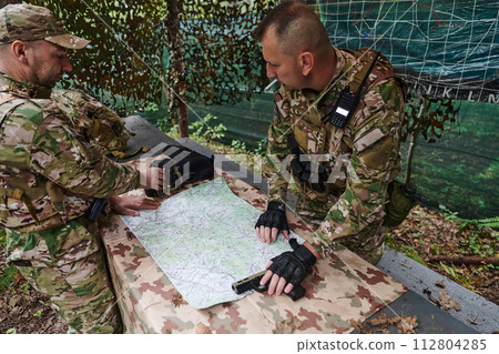 A highly trained military unit strategizes and organizes a tactical mission while studying a military map during a briefing session A highly trained military unit strategizes and organizes a tactical mission while studying a military map during a briefing session 112804285