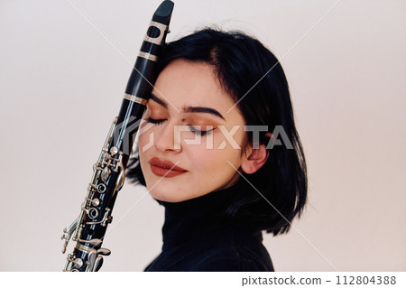 Graceful Brunette Musician Posing with Clarinet on White Background 112804388