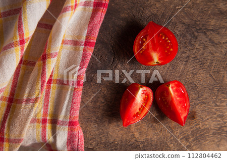 Cut pink tomato and red towel on wooden background.. Cut pink tomato and red towel on wooden background.. 112804462