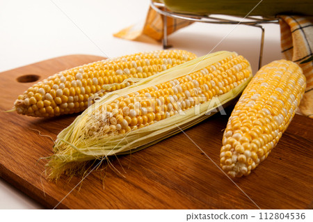 Cutting board with three cobs sweet corn on white wooden background.. Cutting board with three cobs sweet corn on white wooden background.. 112804536