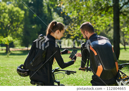 A sweet couple, equipped with bicycles and engrossed in coordinating their journey, checks their GPS mobile and watches while planning scenic routes in the park, seamlessly blending technology and A sweet couple, equipped with bicycles and engrossed in coordinating their journey, checks their GPS mobile and watches while planning scenic routes in the park, seamlessly blending technology and 112804665