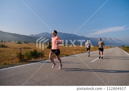 A group of friends maintains a healthy lifestyle by running outdoors on a sunny day, bonding over fitness and enjoying the energizing effects of exercise and nature 112804917