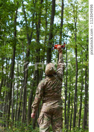 Elite military unit, equipped with state-of-the-art technology including a drone, strategically navigates and surveys dangerous wooded terrain, showcasing their precision, cooperation, and specialized Elite military unit, equipped with state-of-the-art technology including a drone, strategically navigates and surveys dangerous wooded terrain, showcasing their precision, cooperation, and specialized 112804996
