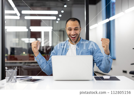 A joyous office worker celebrates a successful moment, displaying a positive reaction with a fist pump in a bright office setting. A joyous office worker celebrates a successful moment, displaying a positive reaction with a fist pump in a bright office setting. 112805156