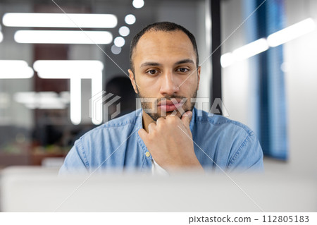 Focused professional man engaged in work at a contemporary office setting with modern lights and clean design. 112805183