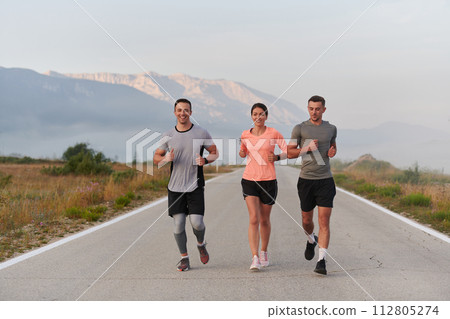 A group of friends, athletes, and joggers embrace the early morning hours as they run through the misty dawn, energized by the rising sun and surrounded by the tranquil beauty of nature 112805274