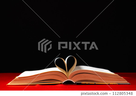 The pages of the book are folded in the shape of a heart on a red and black background, place for text 112805348