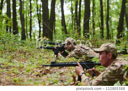 Elite soldiers stealthily maneuver through the dense forest, camouflaged in specialized gear, as they embark on a covert and strategic military mission 112805388