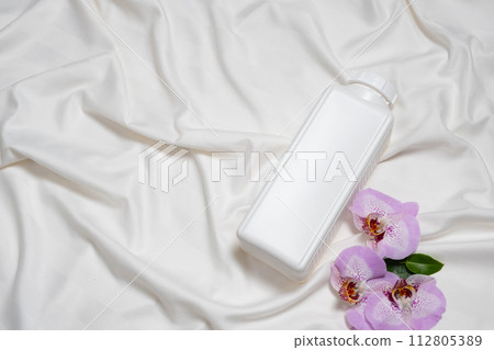 Washing liquid or fabric softener on bed linen with orchid flowers, top view 112805389
