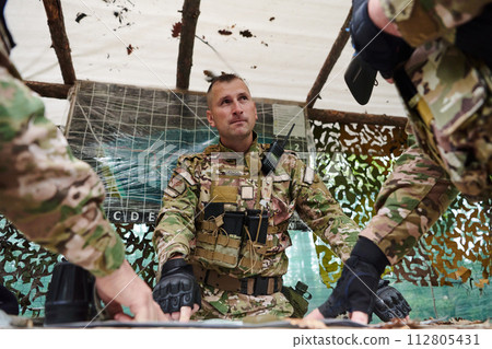 A highly trained military unit strategizes and organizes a tactical mission while studying a military map during a briefing session A highly trained military unit strategizes and organizes a tactical mission while studying a military map during a briefing session 112805431