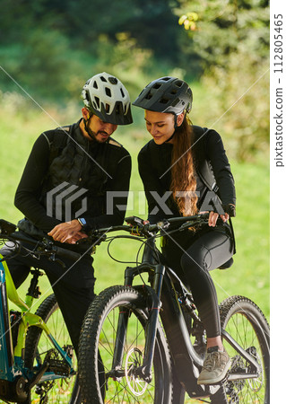 A sweet couple, equipped with bicycles and engrossed in coordinating their journey, checks their GPS mobile and watches while planning scenic routes in the park, seamlessly blending technology and A sweet couple, equipped with bicycles and engrossed in coordinating their journey, checks their GPS mobile and watches while planning scenic routes in the park, seamlessly blending technology and 112805465