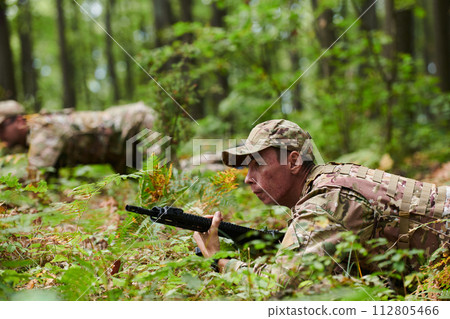 Elite soldiers stealthily maneuver through the dense forest, camouflaged in specialized gear, as they embark on a covert and strategic military mission Elite soldiers stealthily maneuver through the dense forest, camouflaged in specialized gear, as they embark on a covert and strategic military mission 112805466