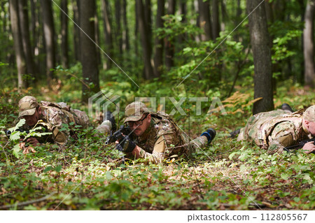 Elite soldiers stealthily maneuver through the dense forest, camouflaged in specialized gear, as they embark on a covert and strategic military mission 112805567