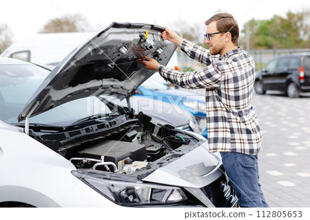 Young man checking under the hood of his car to figure out what the problem is. Young man checking under the hood of his car to figure out what the problem is. 112805653