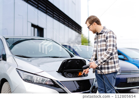 Young man plugging charging cable into the car socket. Electric car charging concept Young man plugging charging cable into the car socket. Electric car charging concept 112805654
