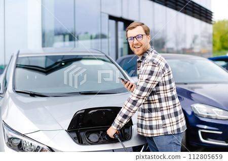 Young man plugging charging cable into the car socket. Electric car charging concept 112805659