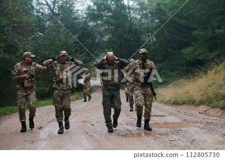 A group of elite soldiers leads captives through a military camp, showcasing a tense atmosphere of detention and security operations 112805730