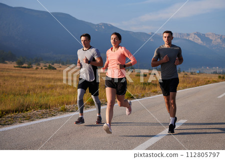 A group of friends maintains a healthy lifestyle by running outdoors on a sunny day, bonding over fitness and enjoying the energizing effects of exercise and nature 112805797
