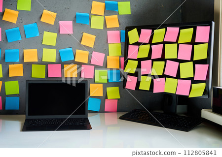 Office workplace with laptop and desktop pc full of blank colorful sticky notes reminders. 112805841