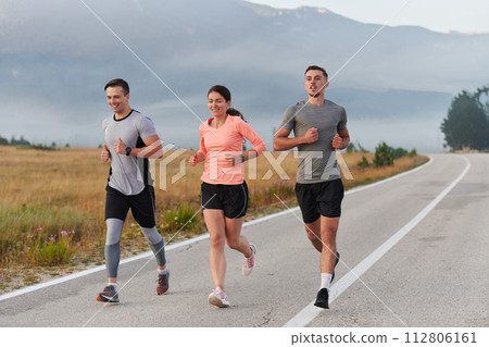 A group of friends, athletes, and joggers embrace the early morning hours as they run through the misty dawn, energized by the rising sun and surrounded by the tranquil beauty of nature 112806161