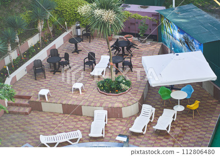 Top view of the hotel territory with white plastic sun loungers, tables and chairs, canopy, trees and palm trees, flowers. Background with copy space. Concept of vacation, honeymoon. Top view of the hotel territory with white plastic sun loungers, tables and chairs, canopy, trees and palm trees, flowers. Background with copy space. Concept of vacation, honeymoon. 112806480