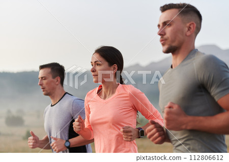 A group of friends, athletes, and joggers embrace the early morning hours as they run through the misty dawn, energized by the rising sun and surrounded by the tranquil beauty of nature 112806612