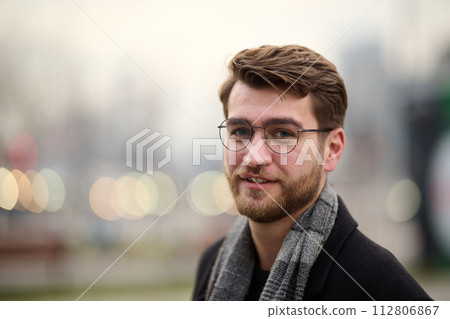 A handsome young man, dressed in a stylish suit, tie, and glasses, exudes the appearance of a serious and confident businessman 112806867