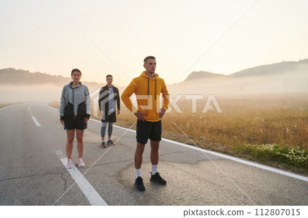 A group of friends, athletes, and joggers embrace the early morning hours as they run through the misty dawn, energized by the rising sun and surrounded by the tranquil beauty of nature A group of friends, athletes, and joggers embrace the early morning hours as they run through the misty dawn, energized by the rising sun and surrounded by the tranquil beauty of nature 112807015