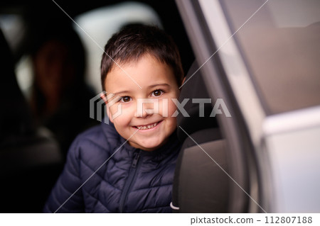 A young boy enjoys a car ride, captured through the window, as he observes the passing scenery. 112807188