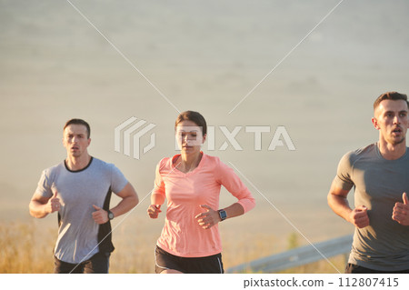 A group of friends, athletes, and joggers embrace the early morning hours as they run through the misty dawn, energized by the rising sun and surrounded by the tranquil beauty of nature 112807415