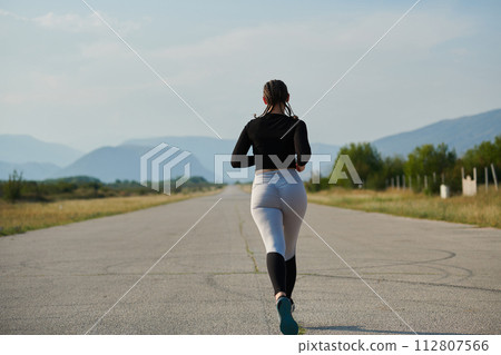 A determined woman athlete trains for success in the morning sun. A determined woman athlete trains for success in the morning sun. 112807566