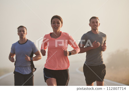 A group of friends, athletes, and joggers embrace the early morning hours as they run through the misty dawn, energized by the rising sun and surrounded by the tranquil beauty of nature 112807714