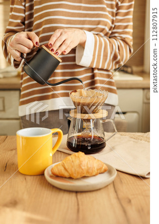 female makes coffee in morning kitchen. brews in purover. yellow cup with black coffee drip female makes coffee in morning kitchen. brews in purover. yellow cup with black coffee drip 112807915