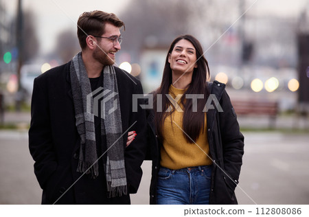 A romantic couple embraces in a tender hug as they stroll through the city streets, enjoying leisure time together in each other's company A romantic couple embraces in a tender hug as they stroll through the city streets, enjoying leisure time together in each other's company 112808086