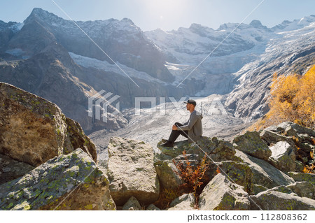 Man sitting on the rock in highest mountains. Mountain with glacier and tourist 112808362