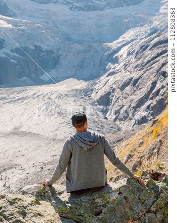 Man sitting on the rock in highest mountains. Mountain with glacier and tourist 112808363