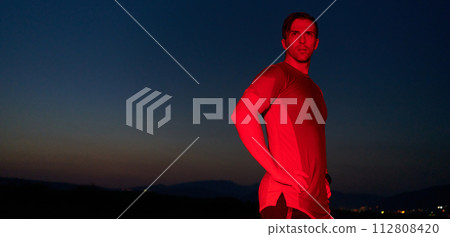 Athlete Strikes a Pose Under Red Nighttime Glow After Intense Daylong Marathon. 112808420