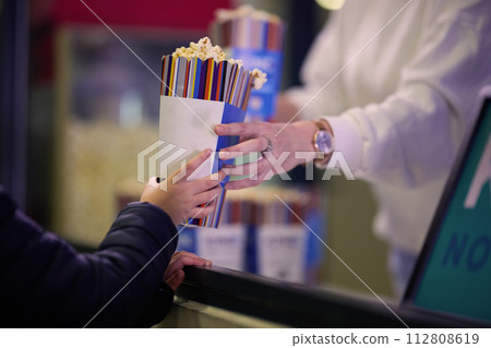 A vendor stands outside the cinema, holding freshly popped popcorn to sell to moviegoers before they enter the theater A vendor stands outside the cinema, holding freshly popped popcorn to sell to moviegoers before they enter the theater 112808619