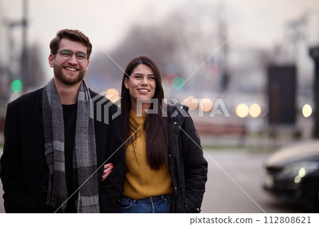 A romantic couple embraces in a tender hug as they stroll through the city streets, enjoying leisure time together in each other's company 112808621