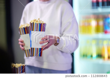 A vendor stands outside the cinema, holding freshly popped popcorn to sell to moviegoers before they enter the theater 112808643