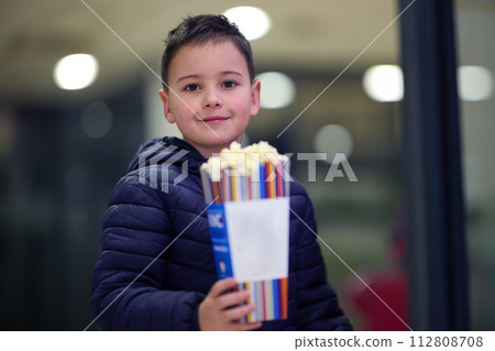 A young boy buys popcorn at the cinema before the start of the movie, his face lit up with excitement. A young boy buys popcorn at the cinema before the start of the movie, his face lit up with excitement. 112808708