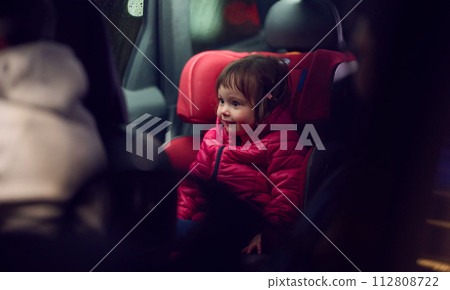 A young girl sits comfortably in a modern car seat, secured and ready for a family adventure on the road. 112808722