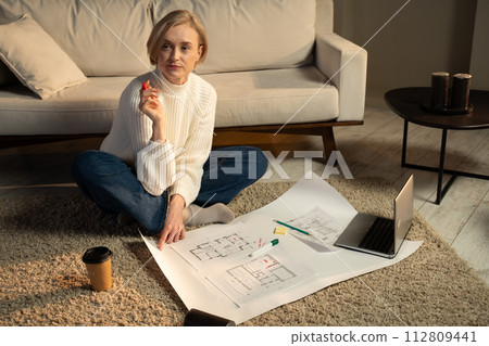 Woman Sketching Architectural Design on Paper in a Cozy Living Room at Evening Woman Sketching Architectural Design on Paper in a Cozy Living Room at Evening 112809441